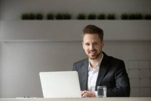 Smiling young businessman in suit with laptop looking at camera